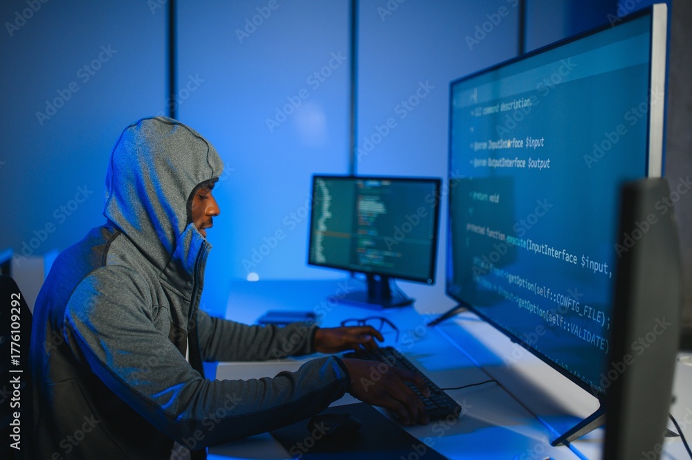 © Serhii - African american Hacker with computer, man sitting at a table in a hoody © Serhii - African american Hacker with computer, man sitting at a table in a hoody