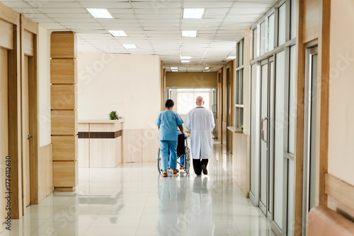 Two healthcare professionals escort a patient in a wheelchair down a bright, clean hospital corridor, reflecting care, safety, and support.