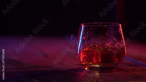 Slow motion shot of ice cubes falling into glass with alcohol on the dark background. Ice cube falling in the glass of whiskey with splash. Copy space.