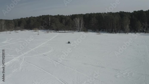 Aerial view from a drone following a woman riding a snowmobile across the expanses of a frozen snowy lake. Winter female extreme sports.