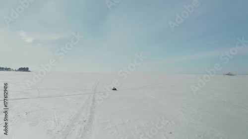 Aerial view from a drone following a woman riding a snowmobile across the expanses of a frozen snowy lake. Winter female extreme sports.