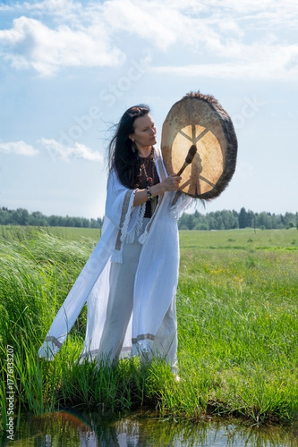 Shaman in the white dress drumming in the natural environment