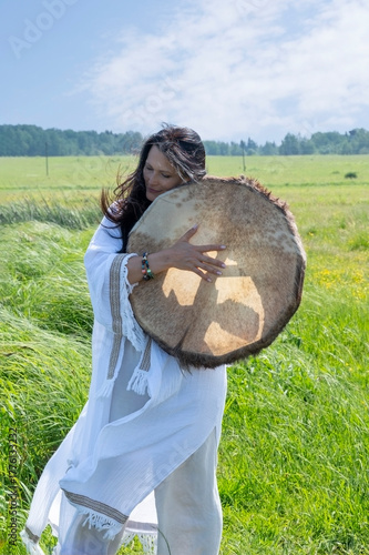 Female shaman in the white dress drumming outdoors