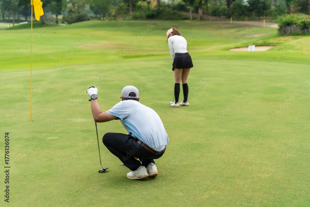 Obraz premium Asian man and woman golfers swing clubs together on scenic golf course.
