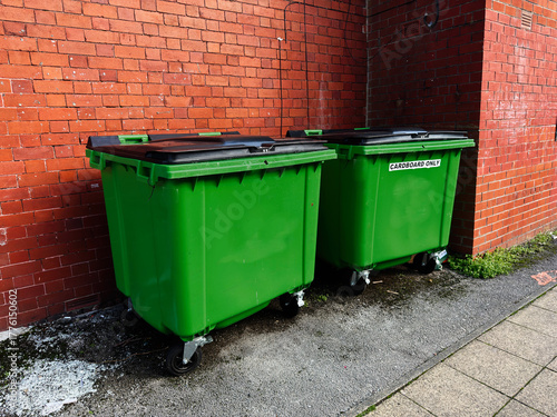 Green waste bins against a red brick wall in Manchester UK near cardboard recycling area
