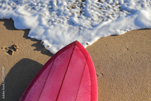 Pink surfboard resting on sand near ocean wave