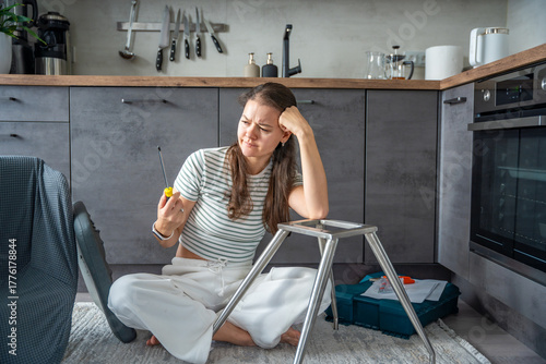 Fotografi Frustrated young woman trying to assemble a chair with tools on the floor