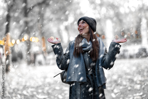 Cheerful smiling woman standing in the snowfall at the park