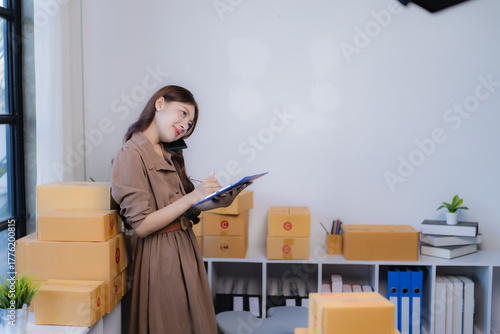 Young woman entrepreneur managing her small business, taking orders on the phone and writing notes while surrounded by shipping boxes from her e-commerce operation