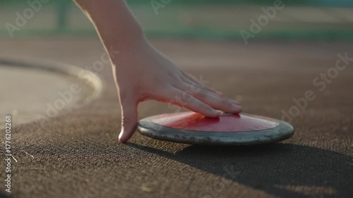 An athlete's hand picks up a close-up of a throwing disc from the floor
