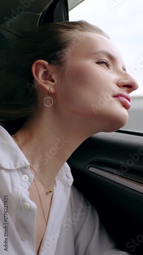 vertical, young woman leans her head out of the car window in slow motion. daytime, she wears make up