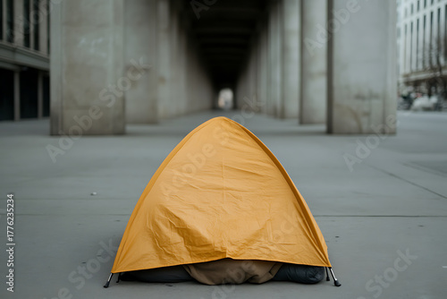 A stark yellow tent sits on the concrete, sheltered by imposing gray pillars and an endless tunnel, highlighting isolation and the struggle of urban survival.