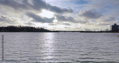 Drone flight over calm lake with ascent revealing a bridge under blue summer sky