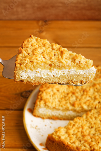 Appetizing close-up of a slice of golden brown streusel pie being lifted with a spatula from the homemade pie, resting on a rustic wooden table. Shallow focus.