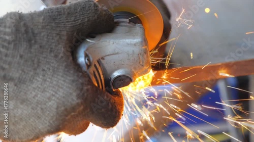Detail view on metal processing with circular saw. Hands of mechanic holding instrument and grinding metal. Worker cutting iron detail in garage or workshop. Bright hot sparks flying around. Close up