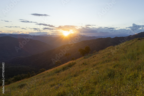 Beautiful serene sunset over grassy mountain hill. Golden light from sun shining over peaceful landscape, creating tranquil and warm feeling of hope and calm