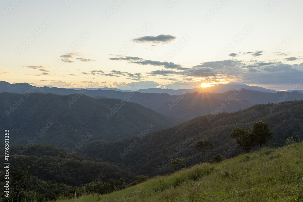 Obraz premium Serene mountain landscape at sunset with beautiful, peaceful view over green valley. sun setting behind cloudy sky creates scenic and tranquil moment in nature