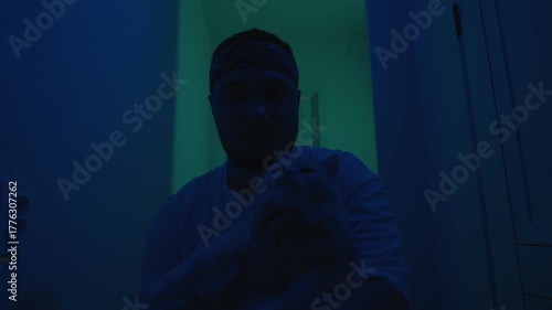 A man with a white cat in his arms, in the hallway, where the lights are blinking.