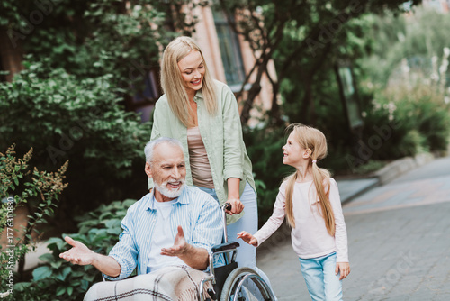 Slika na platnu A heartwarming family walk scene with grandpa in a wheelchair being supported by