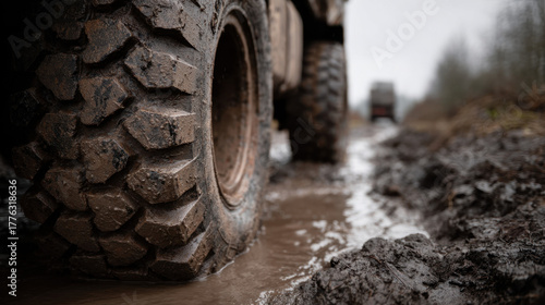 Close-up of heavy truck tires covered in mud driving through deep puddles on a rough dirt road