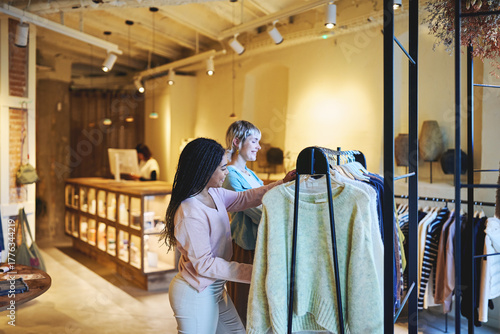 Friends shopping for sweaters in stylish urban clothing boutique