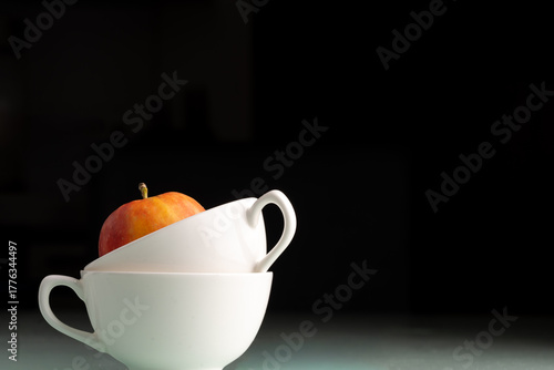 apple sitting in  stack of white coffee mugs isolated