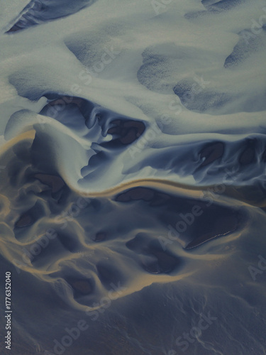 Aerial view of glacial river patterns weaving intricate designs across the landscape, a ballet of textures and tones painting the South Coast, Iceland.