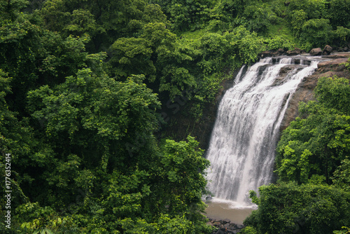 Scenic waterfall near Kasara cascading down rocky cliffs, surrounded by dense green forest during monsoon season.