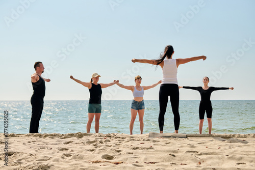 Yoga coach leading group yoga practice on Sandy Beach by Baltic Sea