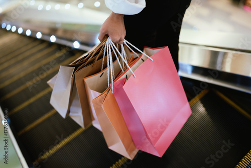 Close-up of a person holding multiple shopping bags in a mall, symbolizing retail therapy, consumerism, and modern lifestyle.