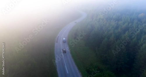 Aerial view of cars driving on winding forest road in morning fog