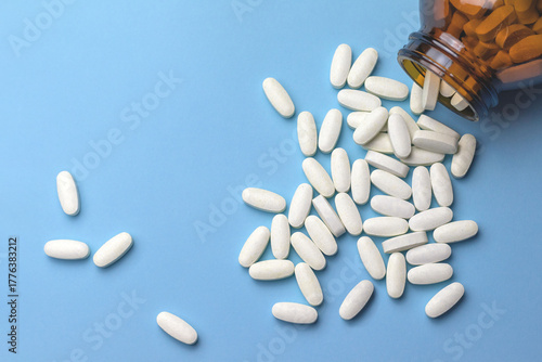 White oval magnesium supplement tablets spill from a brown glass bottle on a blue background. Health and self-care concept.Essential vitamins and minerals for humans.