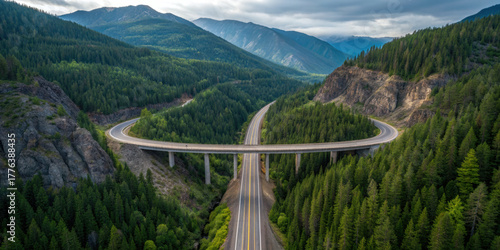 Aerial view of scenic highway bridge curving through lush green forested mountains, under cloudy sky