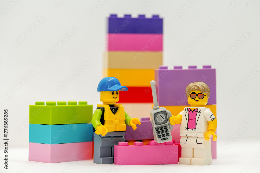 Obraz premium LEGO minifigures: A businessman with a mobile phone and a construction worker stand next to LEGO bricks on a white background.