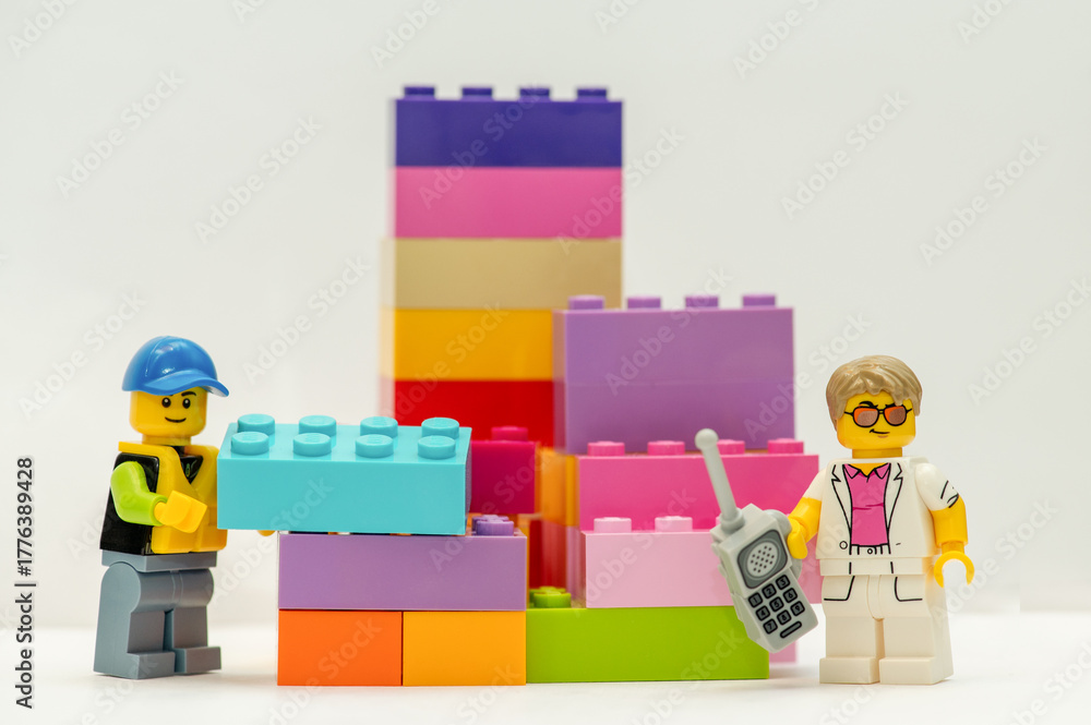 Naklejka premium Lego minifigures with bricks. A businessman with a mobile phone and a construction worker standing next to multi-colored bricks on a white background.