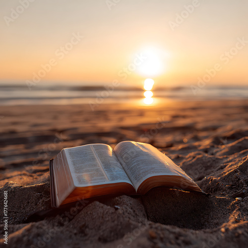 Open Bible resting on sandy beach at sunset with ocean view  