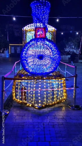 New Year's light installation in the form of a steam locomotive, decorated with many bright lights and garlands with blue, gold and red lights on the background of the night city.