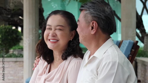 Happy smiling Asian senior couple, elderly husband and wife talking or chatting in urban park rest area with good quality of life togetherness after retirement, real human, real people model