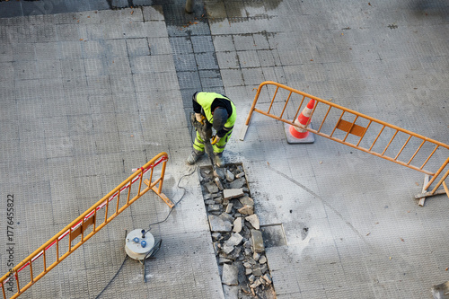 A worker breaks up the sidewalk tile floor with a jackhammer.