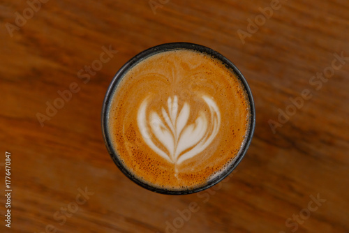 Top-down view of a cappuccino featuring intricate floral latte art on a rustic wooden surface.