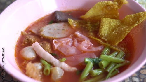 A bowl of Thai Yen Ta Fo noodle soup with pink broth, fish balls, fried wonton, morning glory, and tofu served in a pink bowl. A popular street food dish in Thailand known for its unique sweet and sou