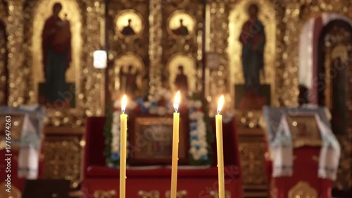 Three church candles burn softly near the baptismal font in an Orthodox temple. The golden light reflects on icons and creates a peaceful, sacred atmosphere of prayer and faith.