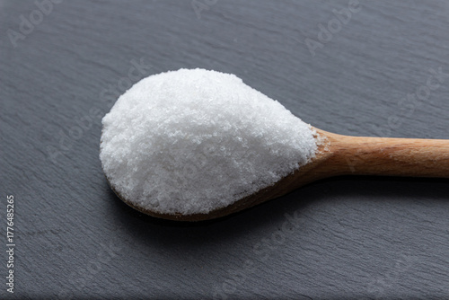 Scoop of iodated salt in wooden spoon in front of dark background. Textured horizontal photo, closeup from above. V27.