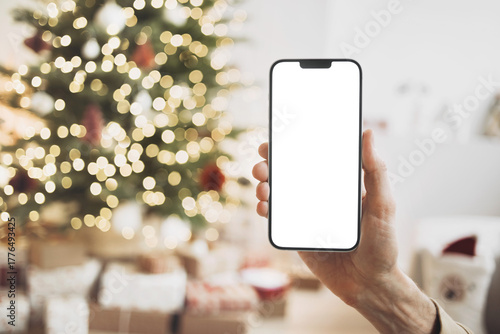 Phone mockup in hand over christmas tree, stars, gifts and decoration, Mobile phone with blank white phone screen isolated transparent PNG, Winter holiday online shopping, xmas 
advertisement concept