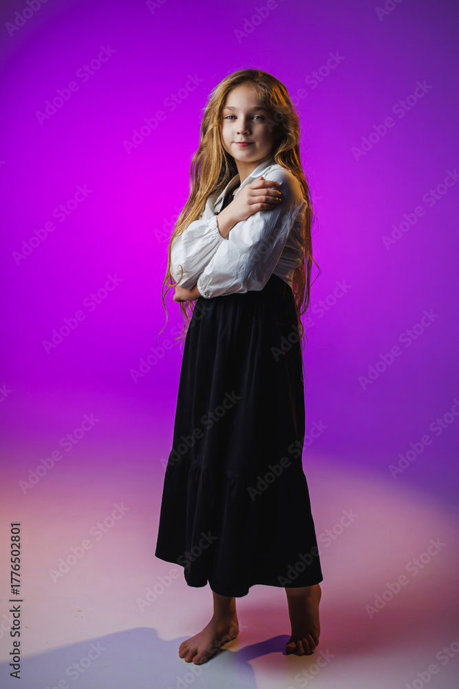 Fototapeta premium Elegant child in black skirt and white blouse standing gracefully in a softly lit purple background showcasing poise and confidence