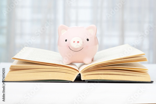 A pink piggy bank is placed on a book and beautiful blurred background. Concept of saving for education.