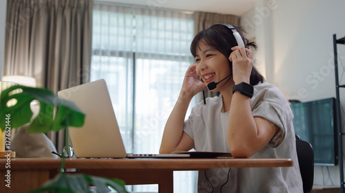 Young Asian girl carefully adjusting her headset microphone while getting ready for an online lesson at home, staying focused and preparing to join her virtual class.