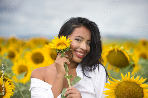 Fotografie A beautiful mulatto Latin woman with a white shirt brings it close to her face and flirts with a sunflower