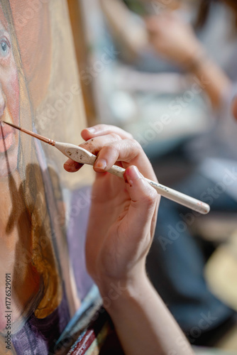 Obraz na plátně Close-up of an artist’s hand painting a portrait on canvas, adding fine details with a brush