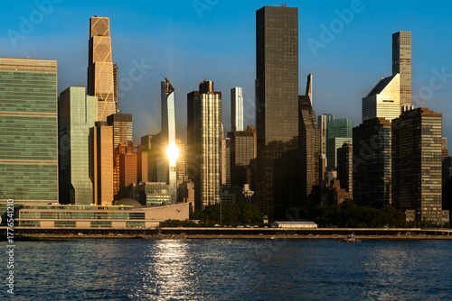 The urban core of Midtown Manhattan, New York, viewed across the East River, with high rise buildings illuminated by the sun.
